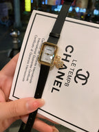 Chanel watch with dark dial, gold-tone case, and black leather strap on card