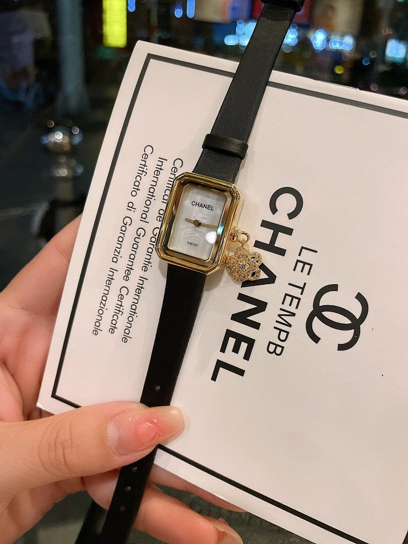 Chanel watch with dark dial, gold-tone case, and black leather strap on card