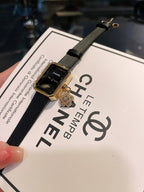 Chanel watch with dark dial, gold-tone case, and black leather strap on card
