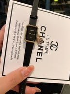 Chanel watch with dark dial, gold-tone case, and black leather strap on card