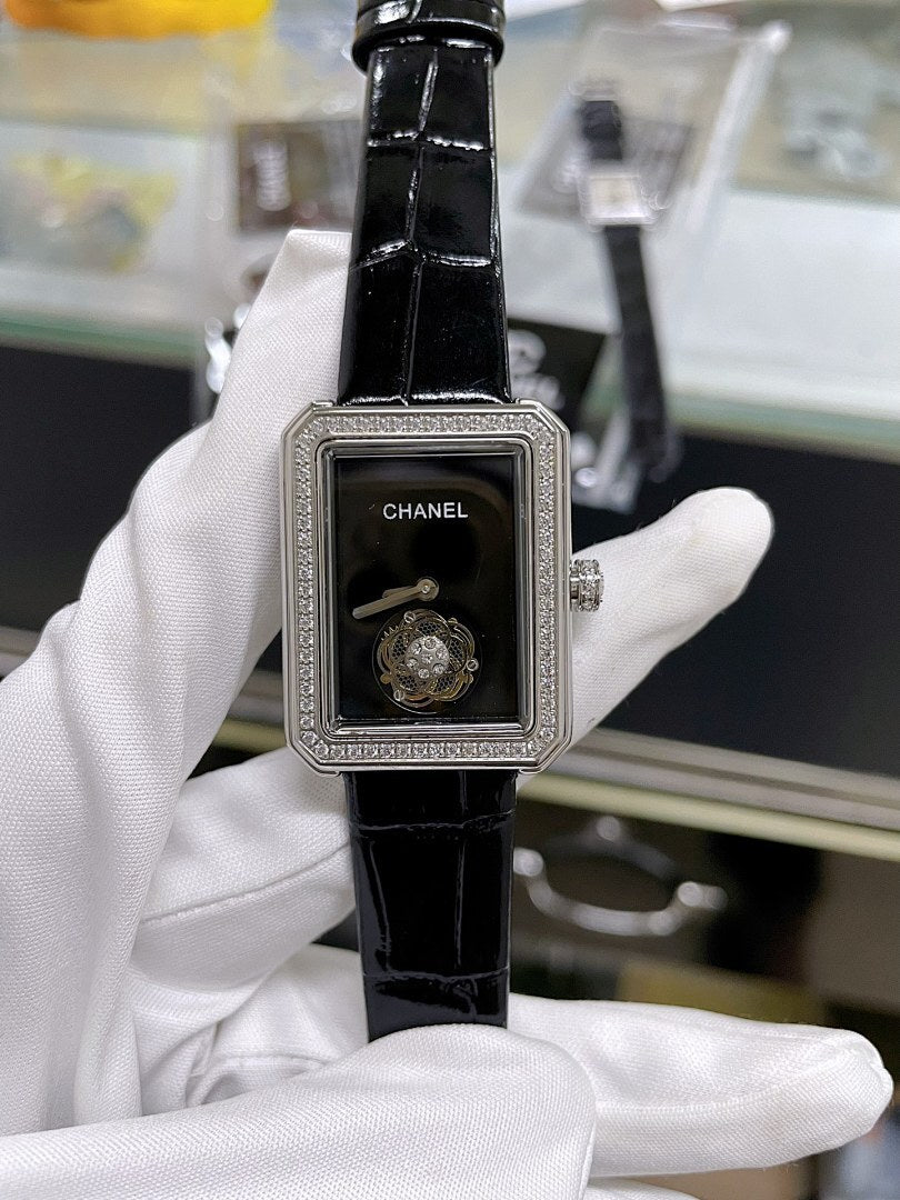 Chanel watch with black leather strap, rectangular case, dark dial with Chanel logo.