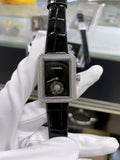Chanel watch with black leather strap, rectangular case, dark dial with Chanel logo.