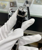 Chanel watch with black leather strap, rectangular case, dark dial, side angle view.
