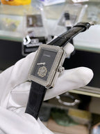 Chanel watch with black leather strap, gemmed rectangular case, dark dial with Chanel logo.