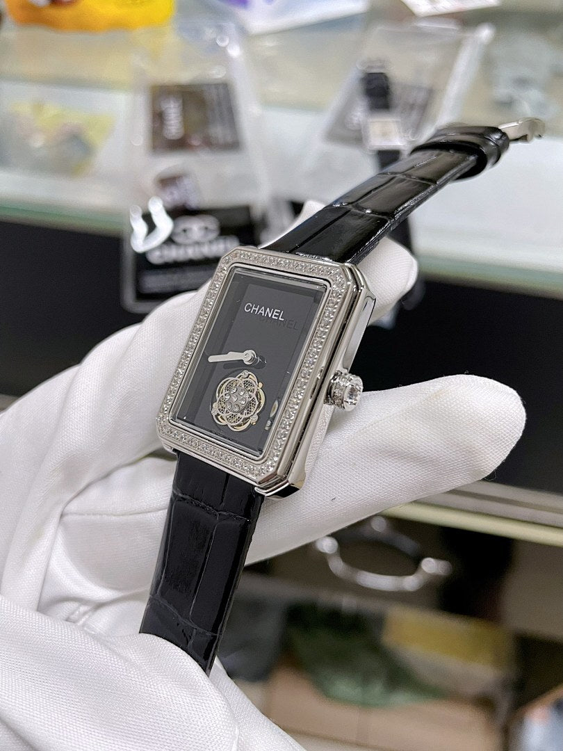 Chanel watch with black leather strap, gemmed rectangular case, dark dial with Chanel logo.