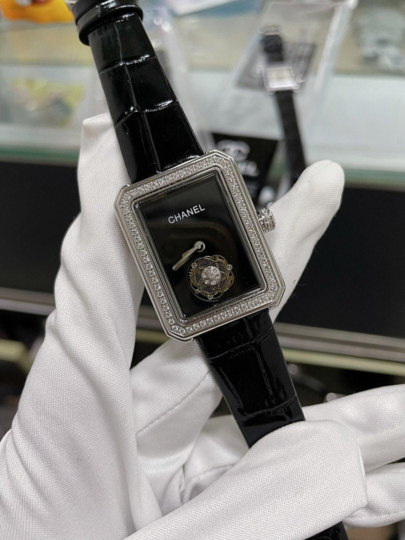 Chanel watch with black leather strap, rectangular silver case, dark dial and Chanel logo.