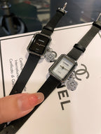Two Chanel watches on black straps with rectangular cases and heart-like charms