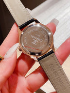 Chanel watch with black leather strap, round silver case and engraved case back.