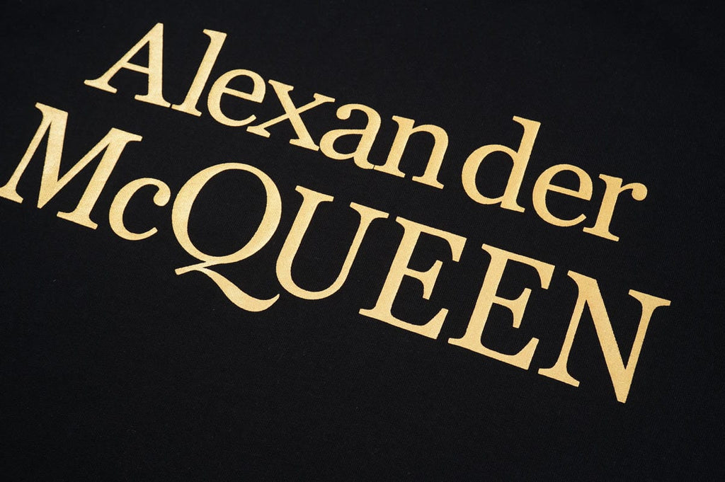 Black T-shirt close-up with gold Alexander McQUEEN logo lettering on chest