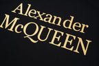 Black T-shirt close-up with gold Alexander McQUEEN logo lettering on chest