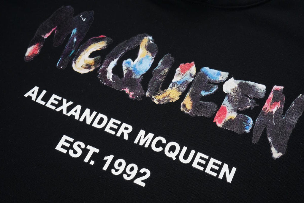 Black pullover hoodie close-up: multicolor “Alexander McQueen EST. 1992” graphic