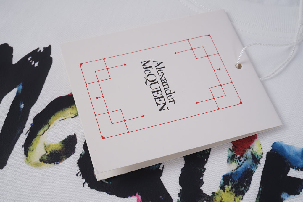 Alexander McQueen clothing tag on white paper with red logo lines and Est. lettering