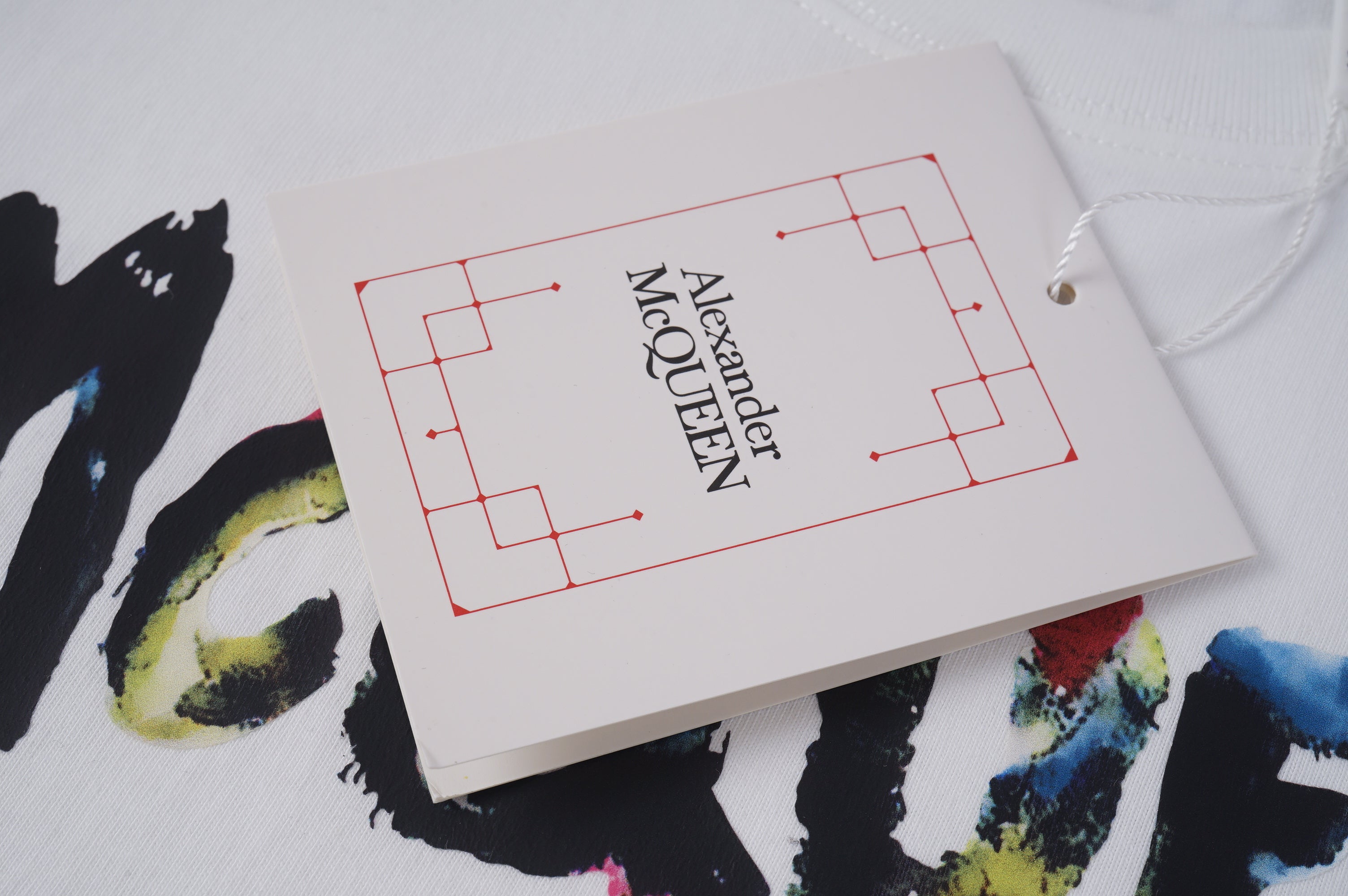 Alexander McQueen clothing tag on white paper with red logo lines and Est. lettering
