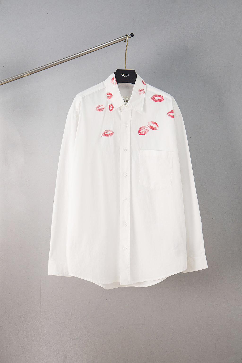White button-up shirt with red lip print, front view on hanger