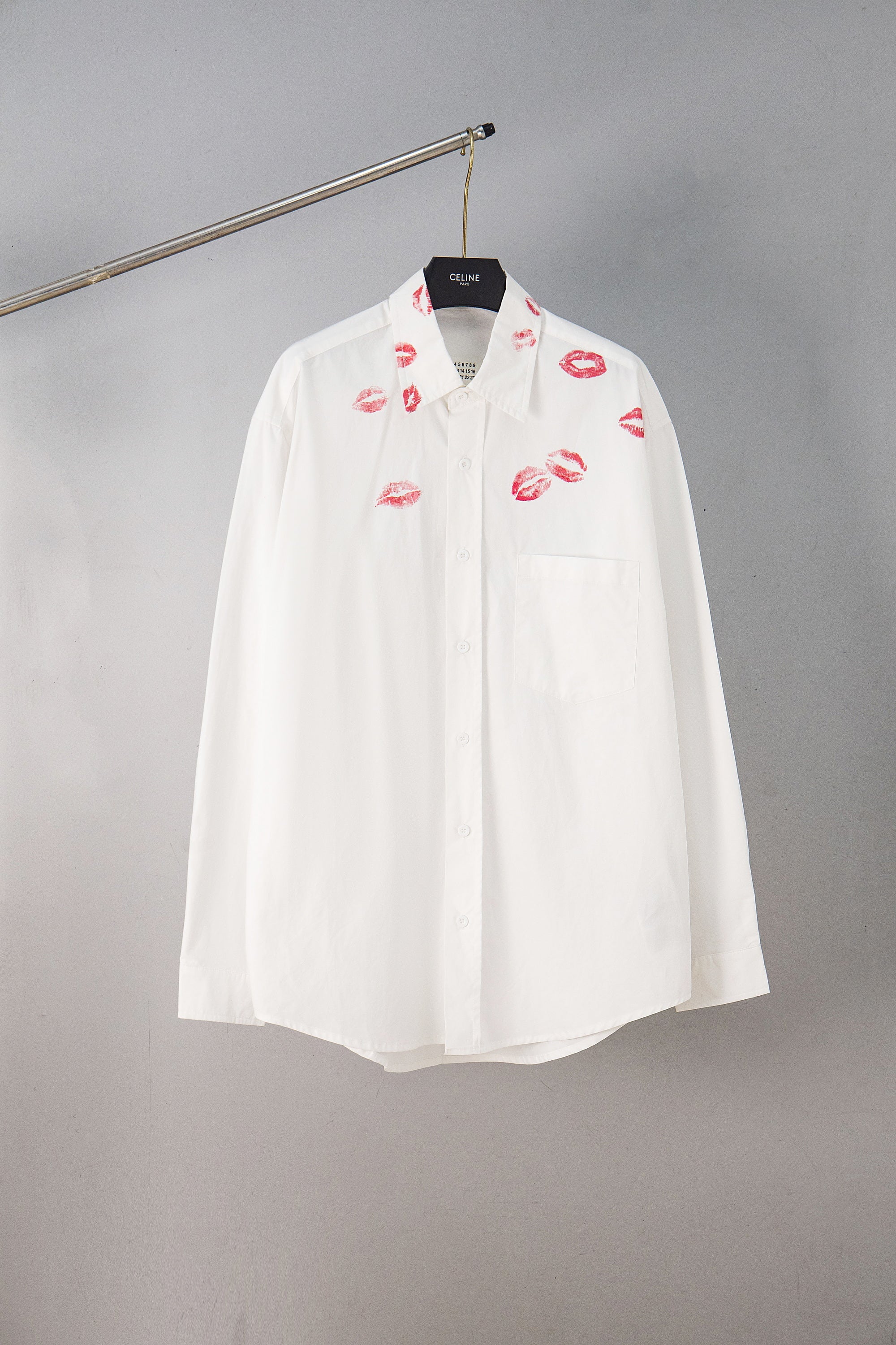White button-up shirt with red lip print, front view on hanger