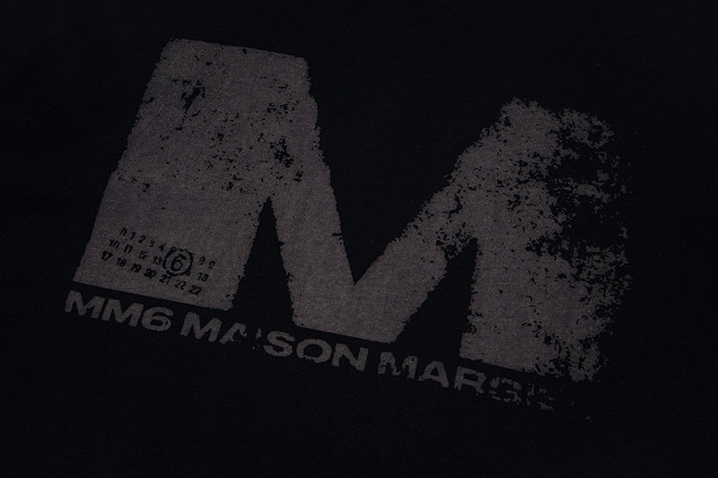Close-up of black graphic T-shirt with distressed M logo print