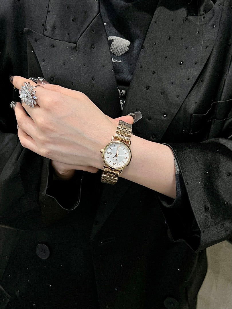 Gold-tone wristwatch with light face and silver metal bracelet on a wrist.