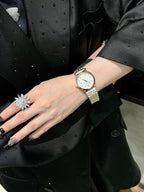 Gold-tone wristwatch with white face and silver metal bracelet, worn with ring jewelry.