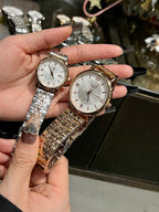 Two wristwatches with silver metal bracelets and white dials held in hand.