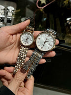 Two wristwatches with silver metal bracelets, one white dial and one light dial, held.