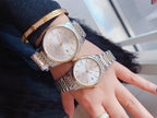 Pair of round stainless steel wristwatches with light dials and metal link bracelets