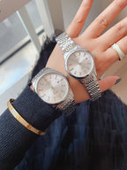 Two round stainless steel wristwatches with light dials and metal link bracelets, side view