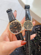 Pair of watches with dark dials and black leather straps, gold-toned cases