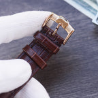 Leather strap wristwatch with gold-tone buckle and dark brown strap, side view