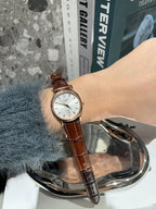 Analog wristwatch with white dial and brown leather strap on wrist