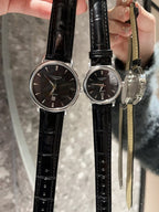 Analog wristwatches with dark dials and black leather straps on hand
