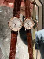 Analog wristwatches with white dials and brown leather straps, gold cases