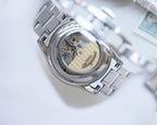 Two-tone stainless steel wristwatch case back with visible movement window