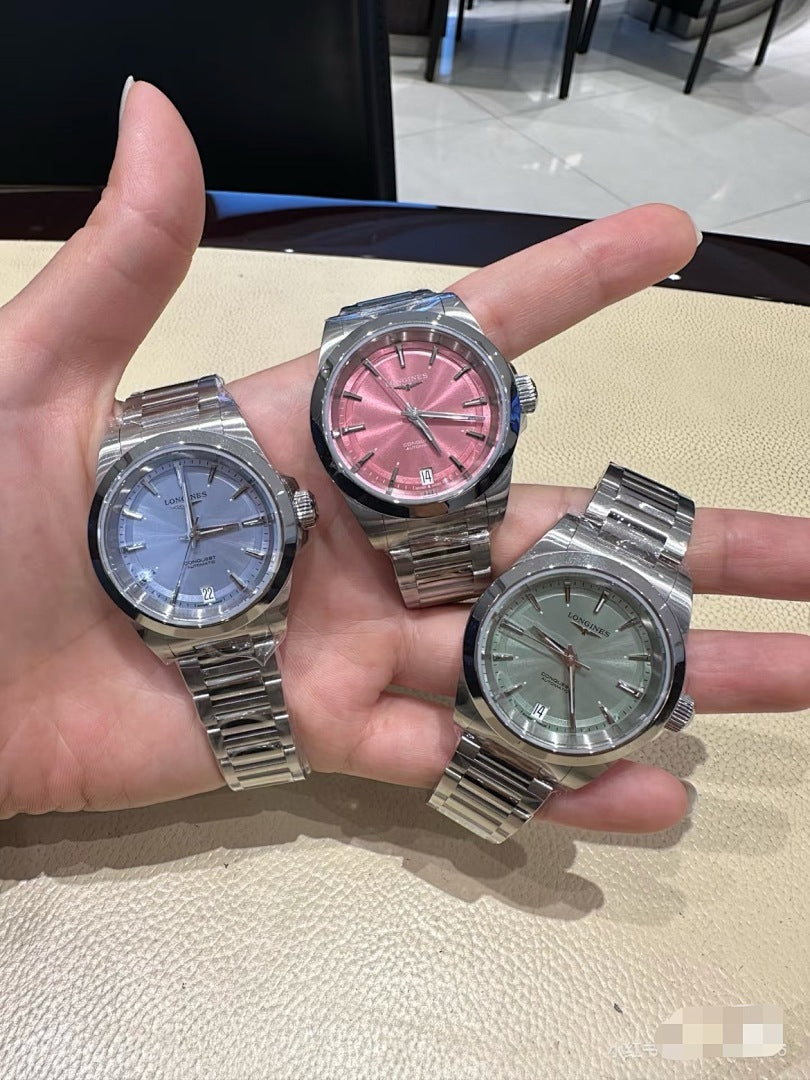 Three stainless steel watches with blue, red-pink, and green dials in hand