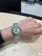 Stainless steel wristwatch with light green dial and metal bracelet on forearm