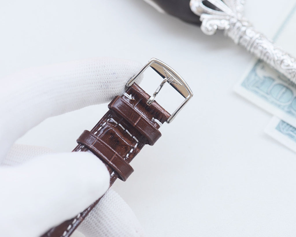 Brown leather watch strap with silver buckle and stitched edges.