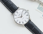 Longines automatic wristwatch, silver-tone case, white dial, black leather strap, angled
