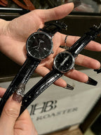 Pair of luxury wrist watches with black leather straps and dark dials