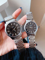 Longines wristwatch, black dial with steel link bracelet, held in hands.