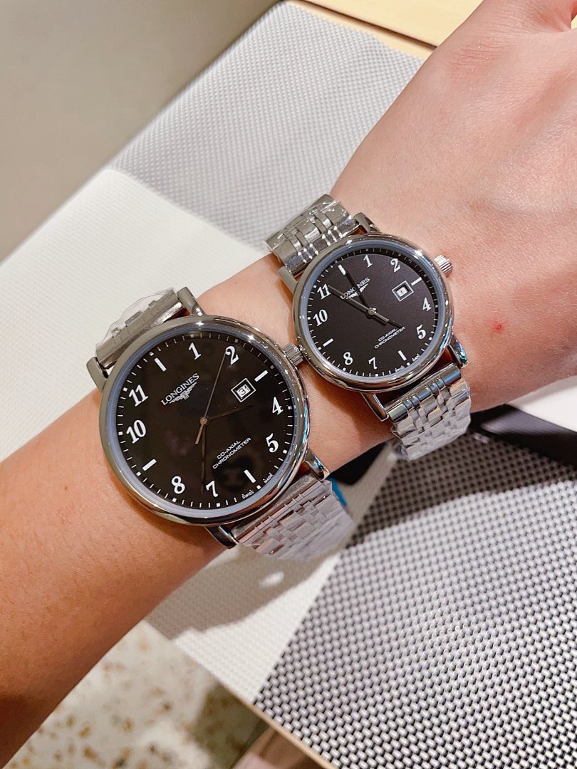 Two silver-tone wrist watches with black dials and metal link bracelets on arm