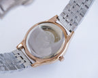 Gold-and-silver watch with metal link bracelet, showing the back of the case