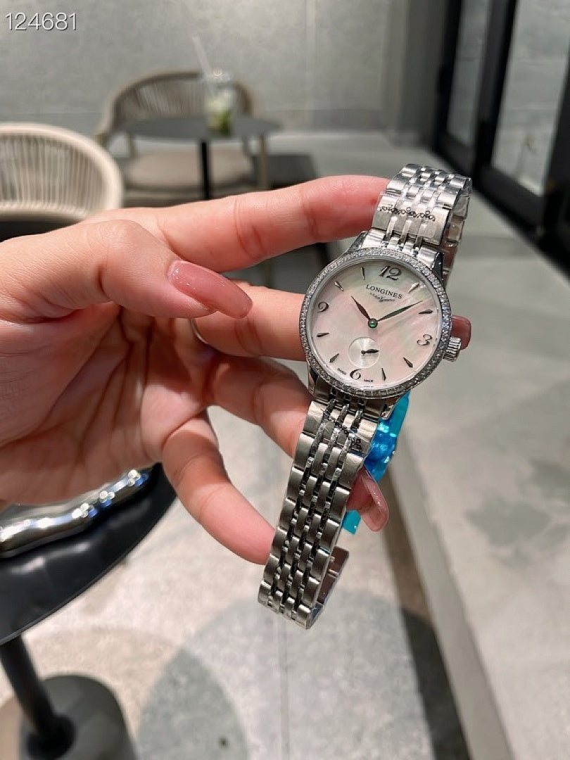 Longines watch held in hand with silver metal bracelet and blue accent detail.