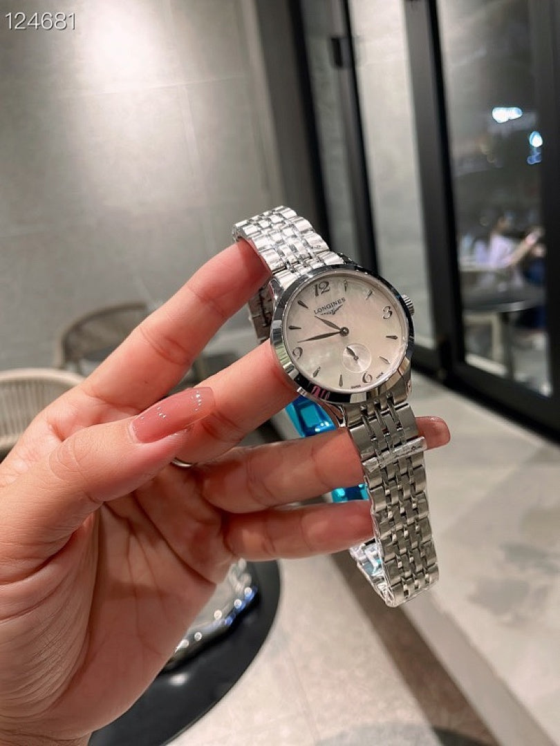 Longines watch held in hand with silver metal bracelet and blue detail on strap.