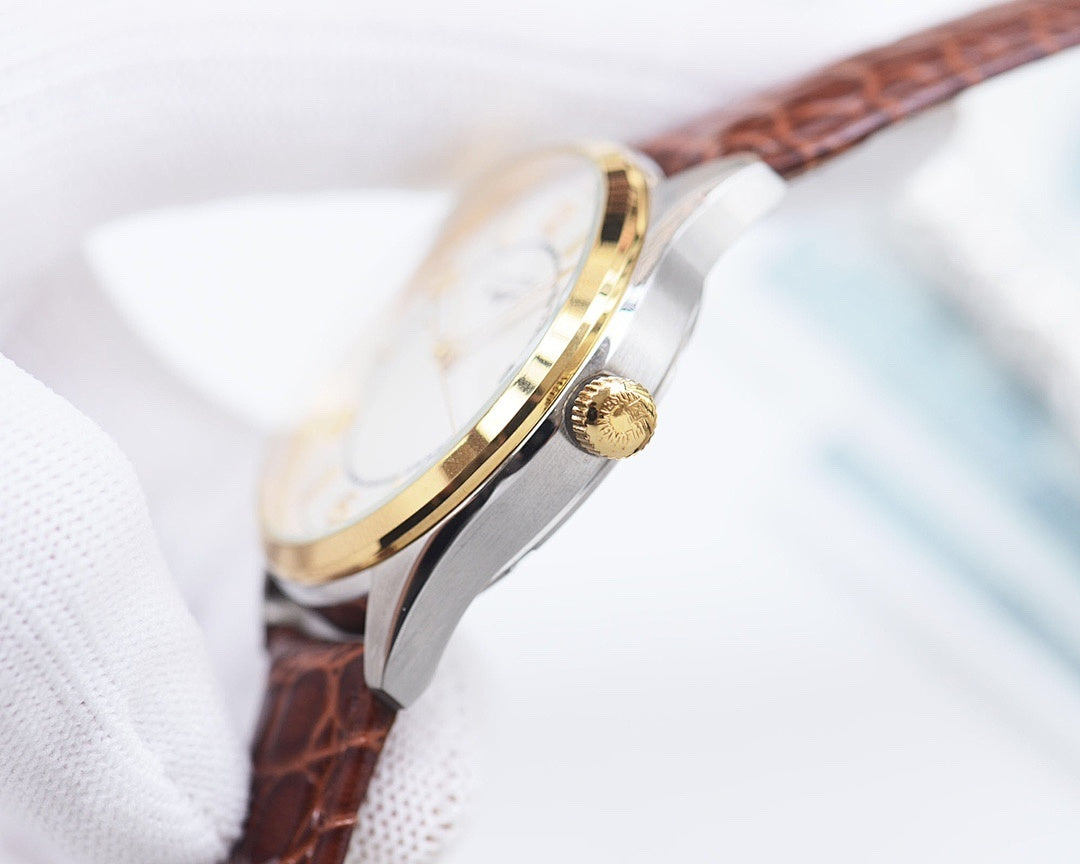 Side view of a gold-capped crown on a silver watch case with brown leather strap.