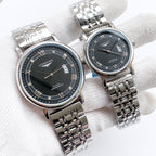 Longines watch with silver metal bracelet, dark dial, Roman numerals and date window.