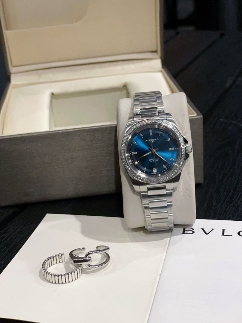 Stainless steel wristwatch with blue dial and metal bracelet on white stand