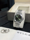 Stainless steel wristwatch with dark green dial and metal bracelet, on white stand