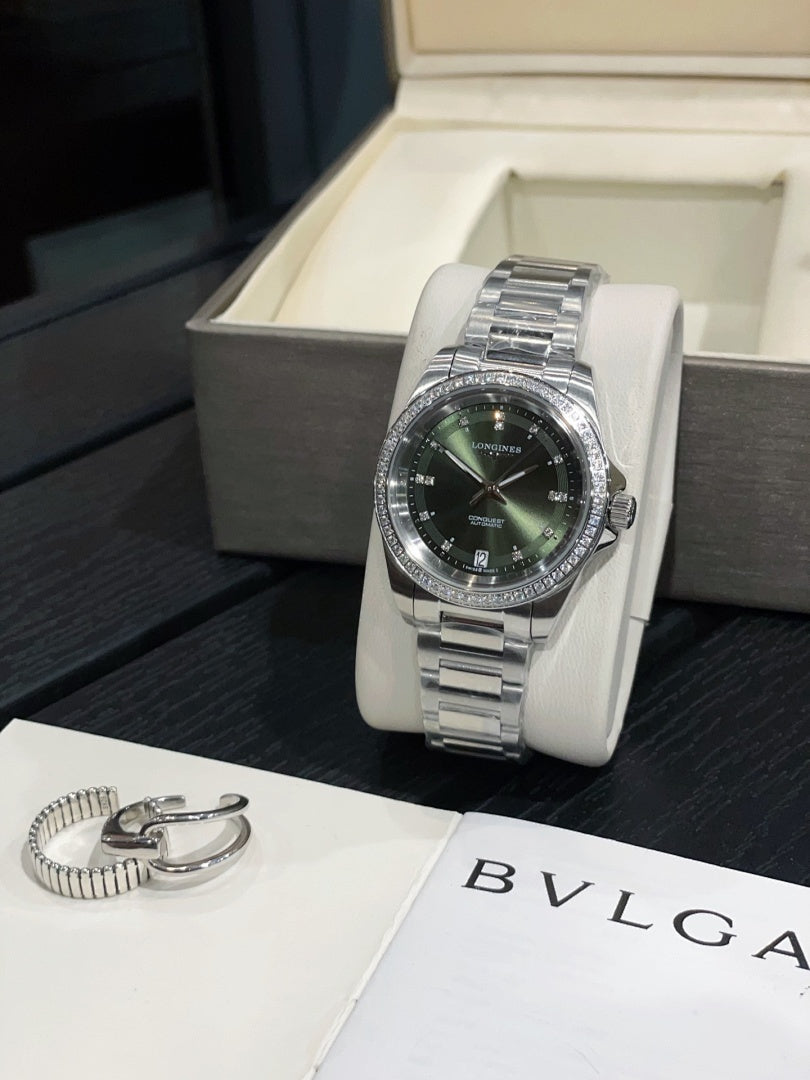 Stainless steel wristwatch with dark green dial and metal bracelet, on white stand