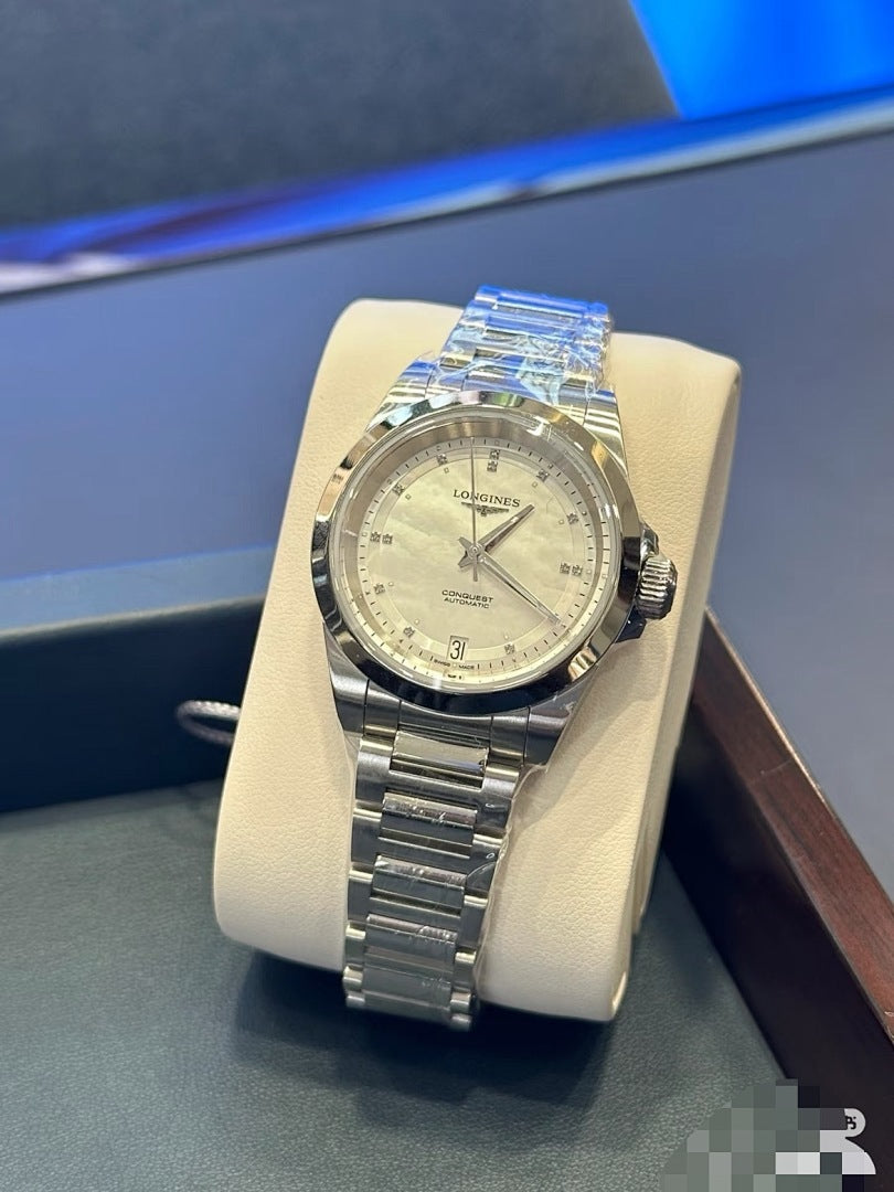 Longines wristwatch with silver metal bracelet and light dial, angled view on stand.