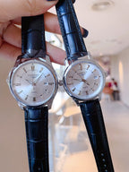Longines watch pair with white dials and black leather straps, held for view.