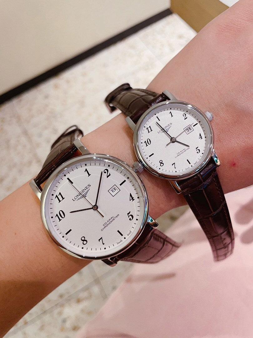 Pair of Longines watches with white dials, brown leather straps, gold-tone cases.